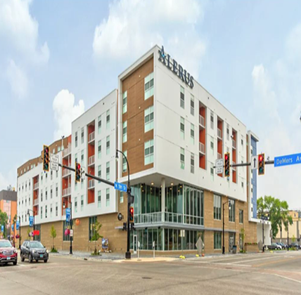 Exterior of Pure North Apartments. Entrance to the first floor grocery store on face the camera. Lots of glass windows on the corner. Building has white and brown siding with red-orange accents.