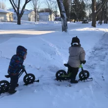 Author Lacey's kiddos snow biking along on the sidewalk in a bunch of snow!