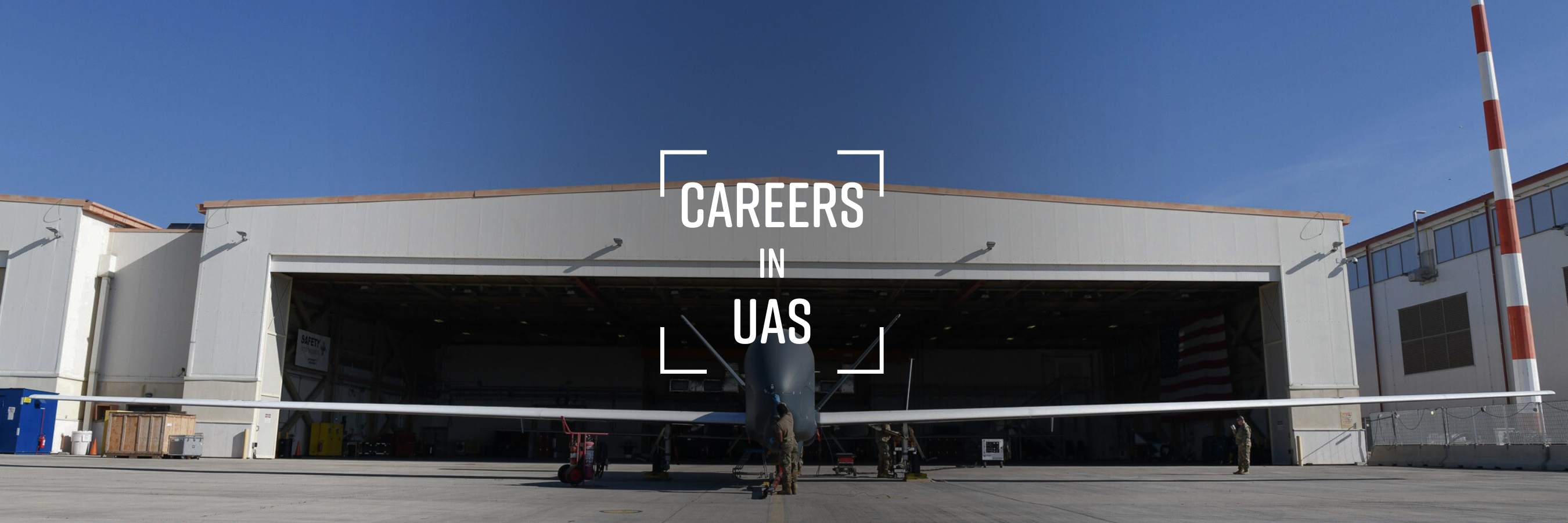 Grand Forks Careers in UAS unmanned and autonomous systems. This is a image of a Global Hawk at a hangar at Grand Forks Air Force Base. A man in a military uniform stands in front of it.