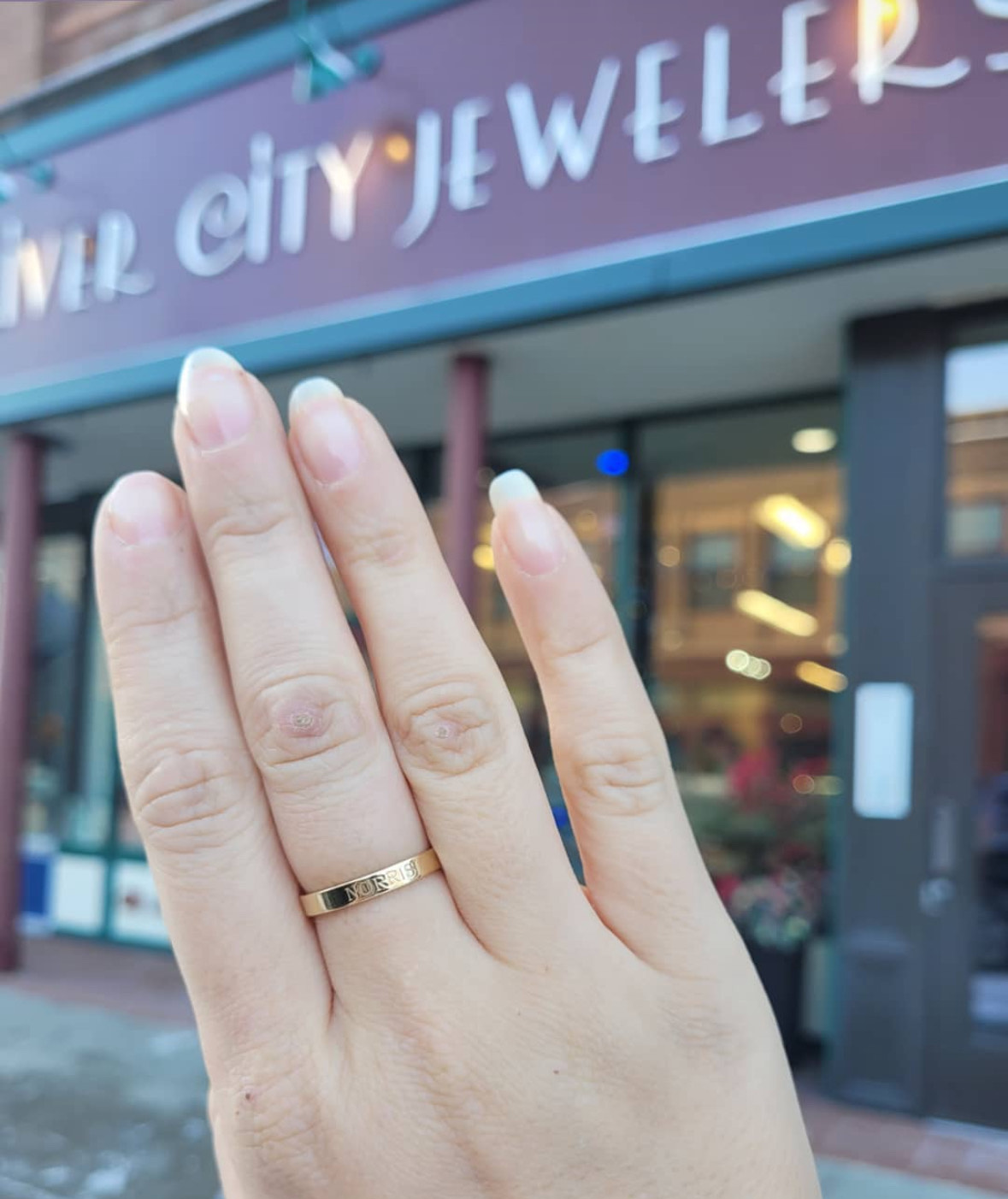 Klaudia Ring Photo Pictured is the authors hand wearing a River City Jewelers "mother" themed ring. She holds up her hand wearing the ring in front of the store.