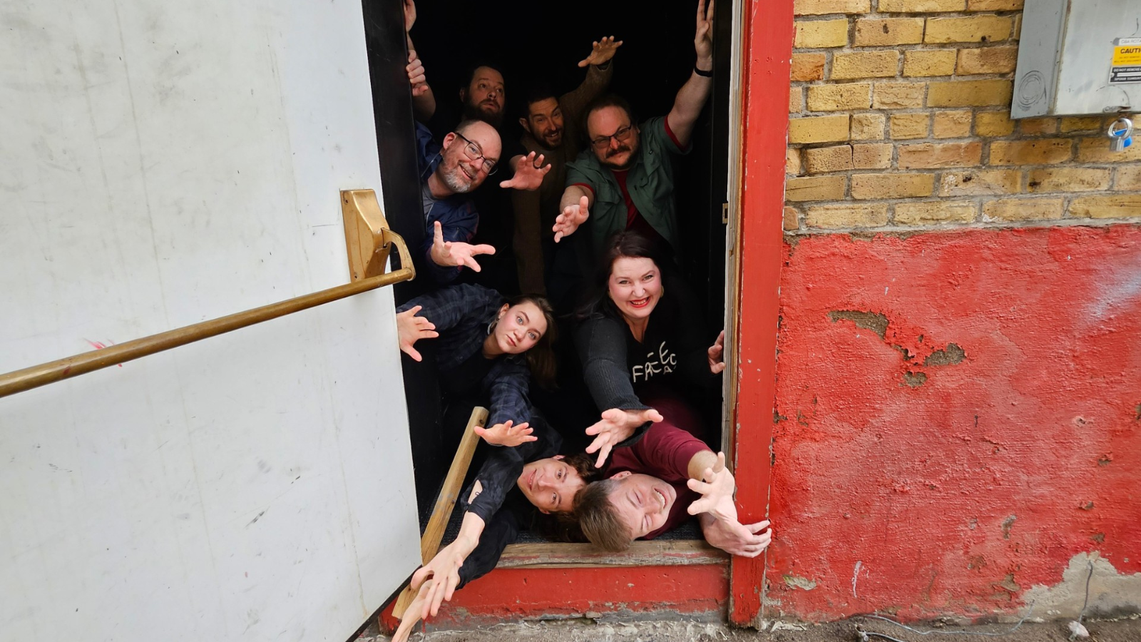 Photo of the Improv Troupe bursting through the firehall theatre door. Author Becca is pictured on the right second from the bottom.