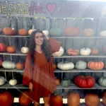 Author Natalie poses in front of the Nelson Pumpkin Patch pumpkin wall in a burnt orange dress.