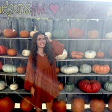 Author Natalie poses in front of the Nelson Pumpkin Patch pumpkin wall in a burnt orange dress.