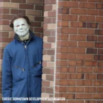 Man in a mask on the downtown walking tour stalks the group from behind the edge of a building