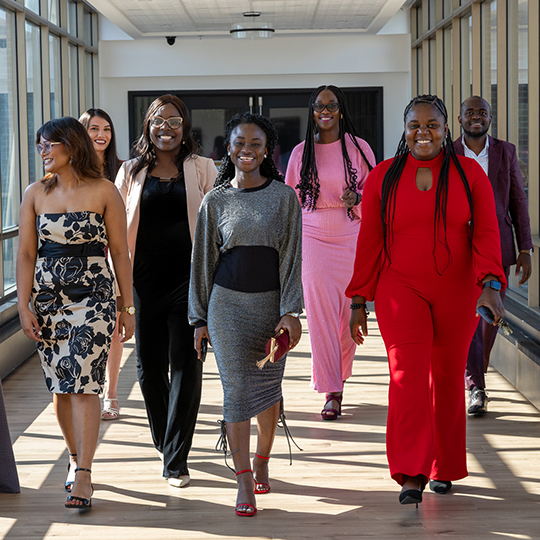 A group of interns catwalk toward the camera with big smiles on dressed to the nines