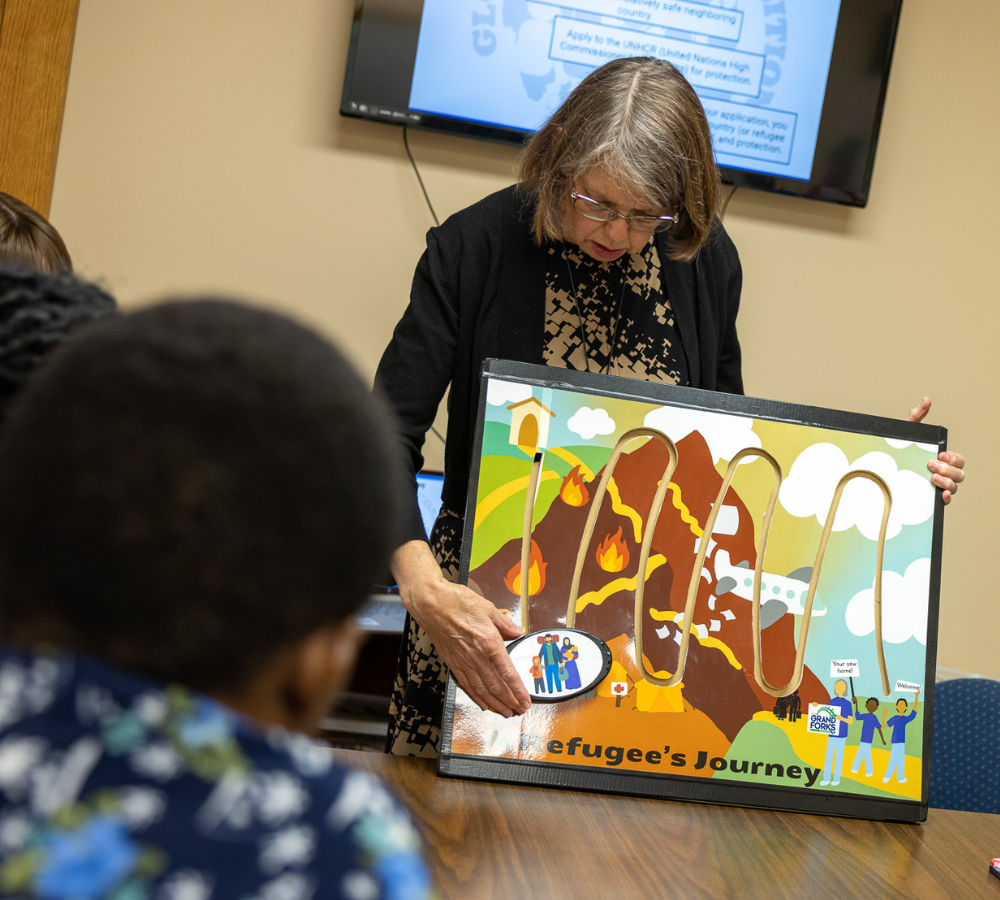 Featured image shows a representative from Global Friends Coalition showing a group of volunteers the refugee's journey via a diagram.