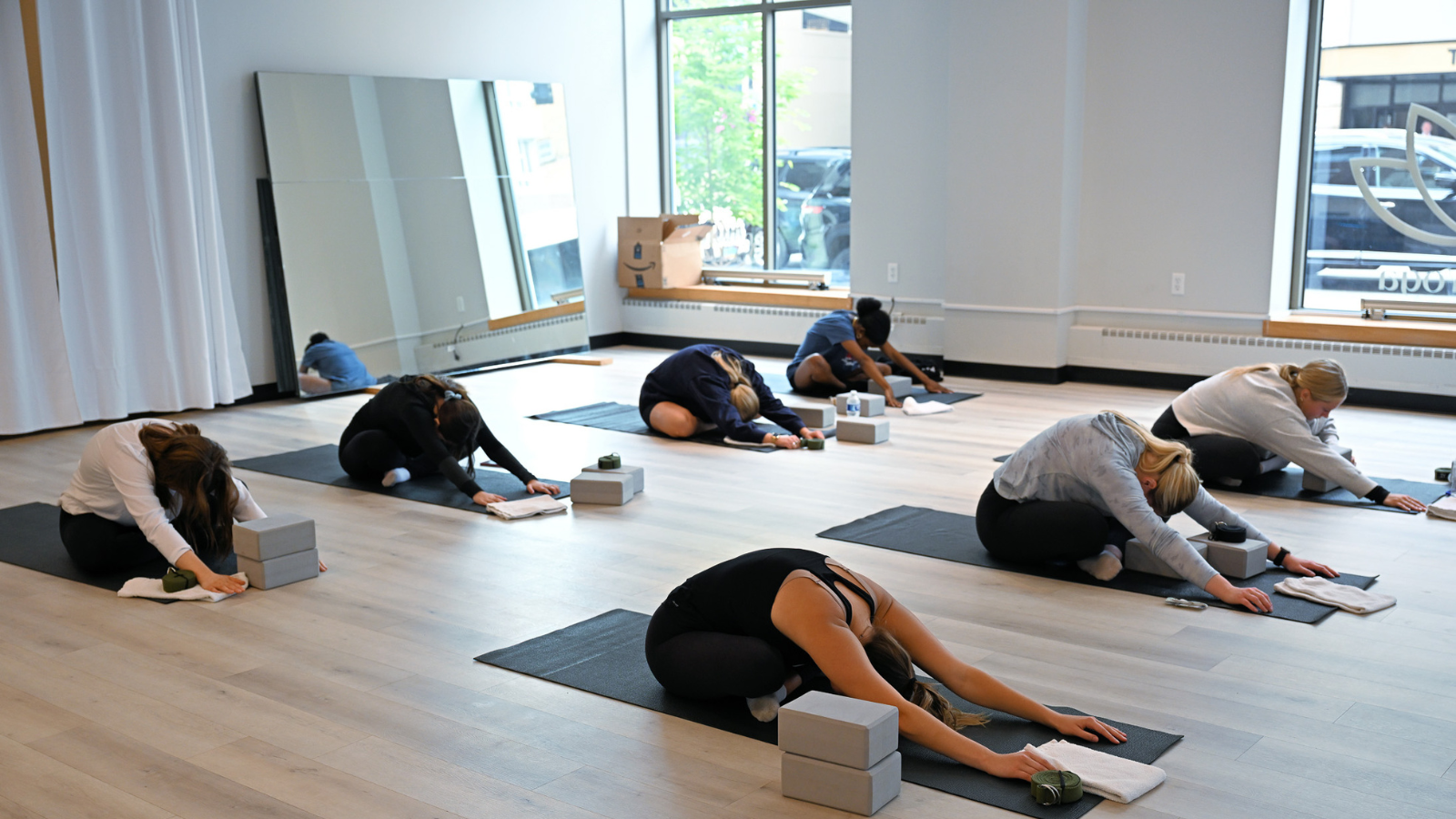Lotus yoga group exercise class leans over their mats together with the daylight pouring in