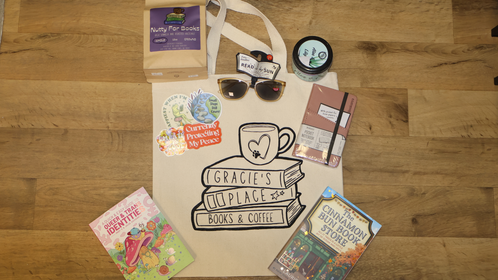 Gracie's Place goodies displayed in a flat lay. A tote bag and a few cozy reads with their store stickers around too!
