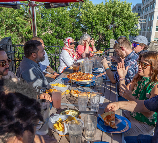A group sits down for some pizza and grub on the Rhombus Pizza rooftop patio in the summertime!