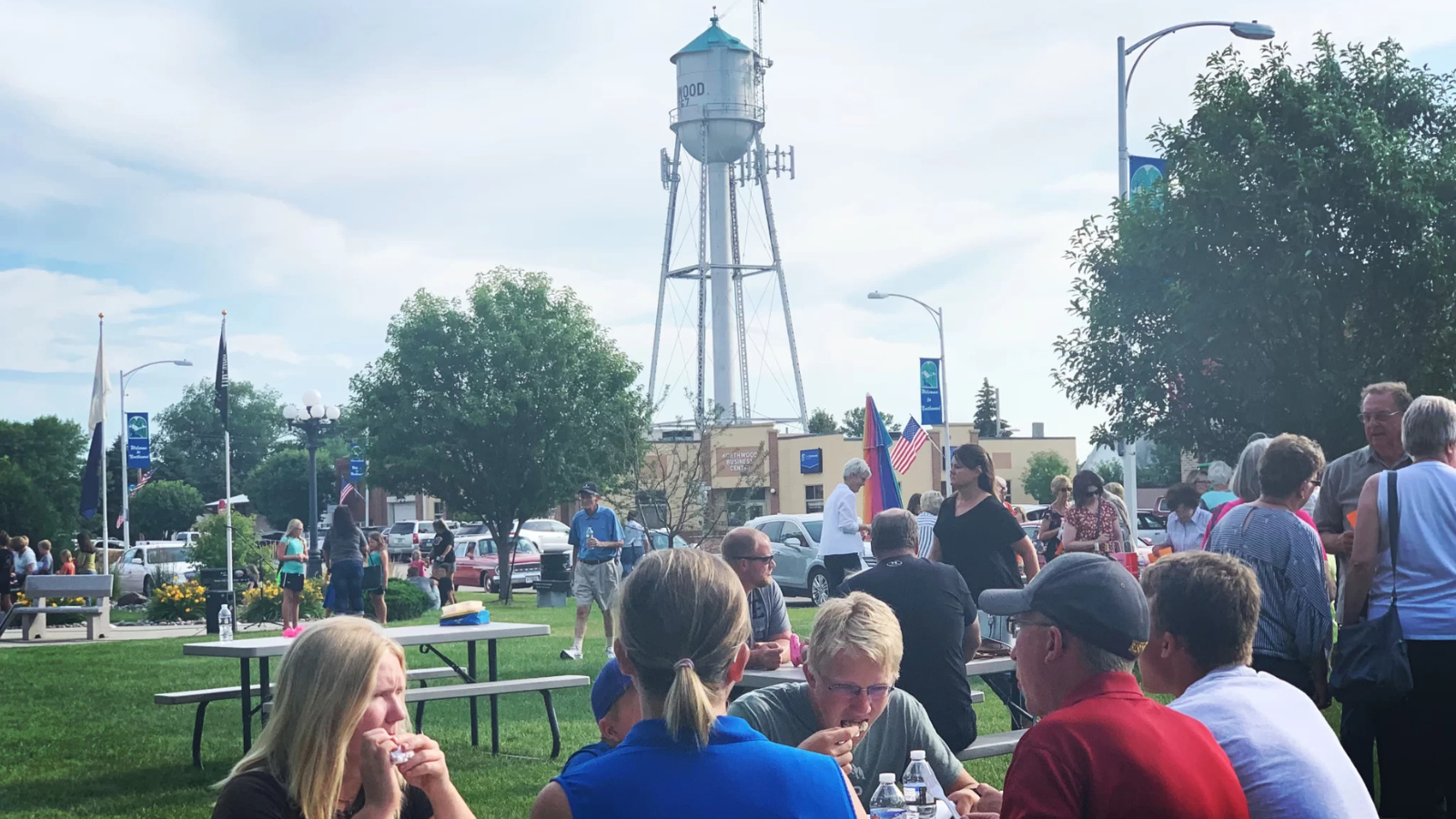 A large crowd of folks in a rural town in Grand Forks county gather at picnic tables to eat!