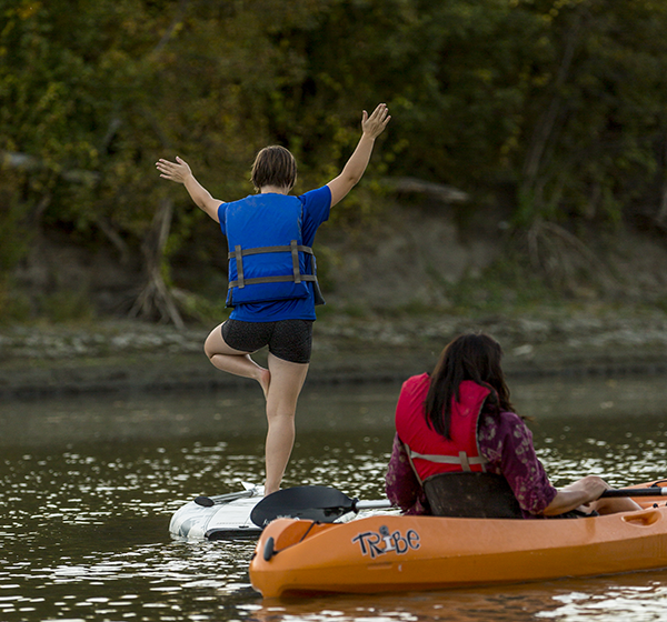 A kayaker and paddle boarder along the Red River take a minute to pause so the paddle boarder strikes a yoga pose on the board