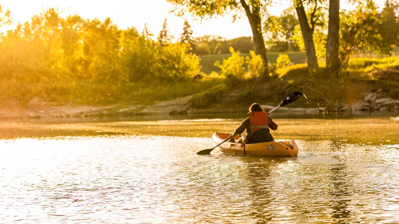 A lone kayaker paddles toward the sunset along the Red River